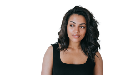 Curious African American girl with perfect wavy hair in black blouse stands at living room looks aside being in good mood. Attractive young Brazilian woman against transparent background. Model