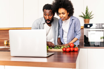Afro american couple cooking at home and learning a recipe online on a computer laptop