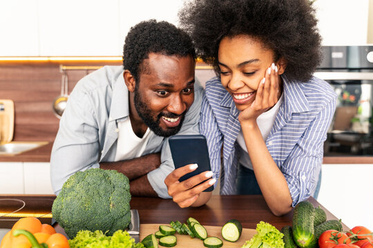 Afro American Couple Cooking At Home And Learning A New Recipe Online On A Cell Phone