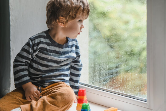 Child playing with colorful toy blocks. Educational toys for young children and looking on the rain drops on the window