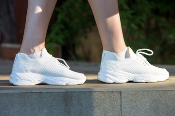 Women's feet shod in white soft sneakers on the sidewalk.