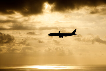 The plane flies over the sea in the sun rays.