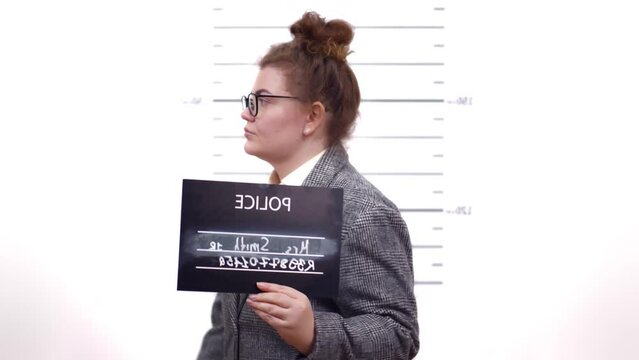 Mugshot of arrested woman holding sign while being photographed in police department. Realtime