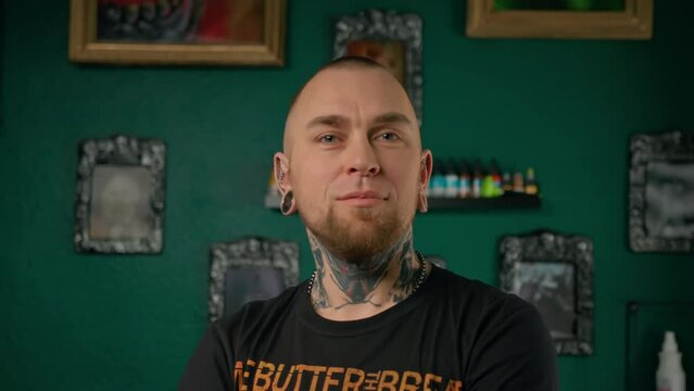 A man with tattoos and piercings looks at the camera - tattoo studio interior