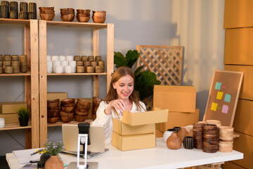 A young pretty woman entrepreneur checking and packaging craft products selling to customers in her shop