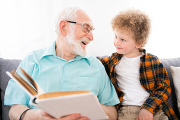 Grandparents and grandson playing at home, grandfater reading a fairytale on a book to his...