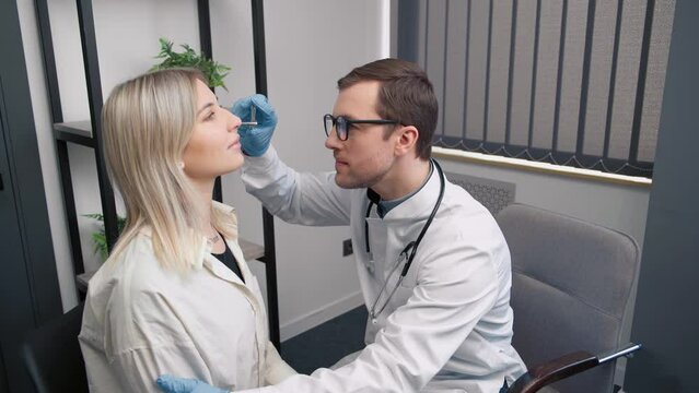 Professional male doctor otorhinolaryngologist doing nose examination with otoscope in modern hospital. Nasal congestion, sinusitis, allergy concept