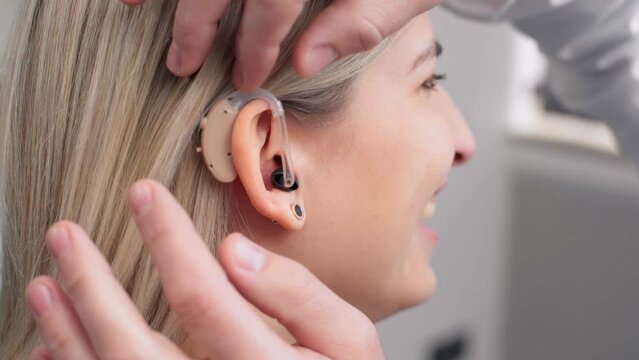 Front view close up of a female patient being fitted with a hearing aid by a doctor
