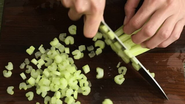 The cook cuts sticks celery on a wooden board.
