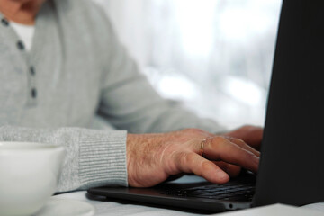 Closeup of senior man hands using laptop. Cropped side view of wrinkled caucasian older hands typing keyboard. Old people with technology. Unrecognizable retired male working from home sitting at desk