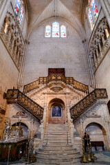 Naklejka premium Escaleras de mármol con una puerta de madera en el centro iluminada por varias vidrieras de colores en el interior de la Catedral de Burgos.