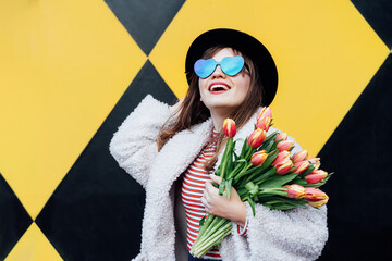 Happy. emotional young fashion woman in heart-shaped sunglasses holding bouquet of fresh tulip...