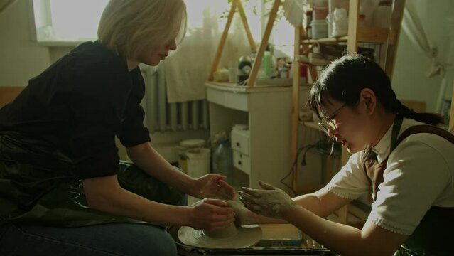 Girl teaching woman in her atmospheric craft workshop pottery studio