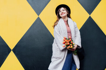 Happy. emotional young fashion woman holding bouquet of fresh tulip flowers on the geometry bright...