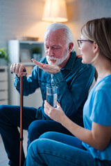 Fototapeta premium Caregiver or nurse giving and showing a pill to senior man on the table. Doctor or nurse caregiver showing a prescrption drug to senior man at home or nursing home. Giving the medicine