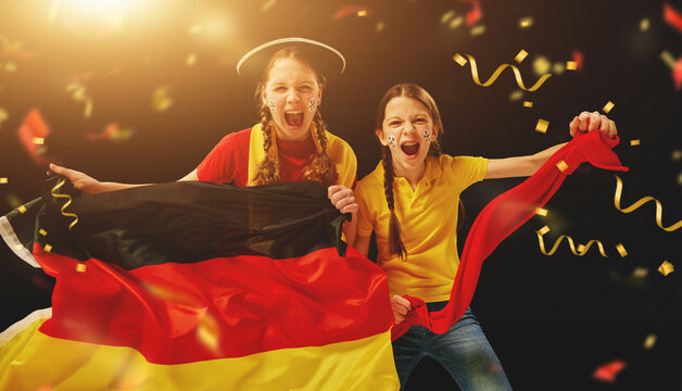 Young girls emotionally watching football match, holding flag and cheering team over dark background with confetti. Concept of sport, leisure time, emotions, hobby and entertainment