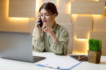 A woman office worker persuades a client on the phone at the workplace.