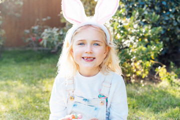 Little girl wearing bunny ears holding opened container with Easter chocolate egg sweets,candies...