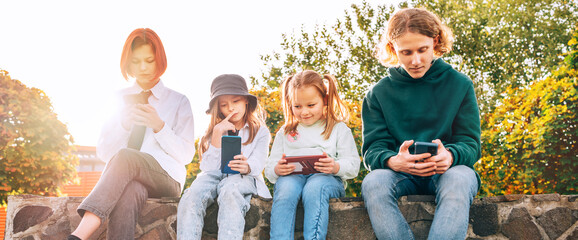 Teenager boy and a sister girls kids sitting and browsing their smartphone devices. Careless young teenhood time and a modern technology concept image.