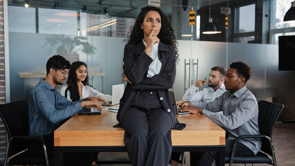 Fototapeta na wymiar Pensive thinking female company CEO thoughtful businesswoman sitting on table office desk in boardroom think multicultural employees multiethnic workers colleagues work meeting brainstorm background