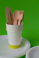 Eco-friendly disposable dishes made of bamboo wood and paper on a green background. Draped spoons, forks, knives, bamboo bowls with paper cups 