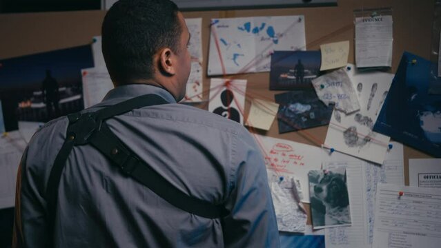 Pensive police detective studying evidence board looking for investigation clues