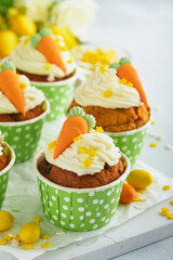 Carrot cake cupcakes for Easter. Carrot cupcakes with cream cheese frosting decorated with tiny marzipan carrots on white background. Happy Easter and spring holiday concept. Holydays homemade dessert