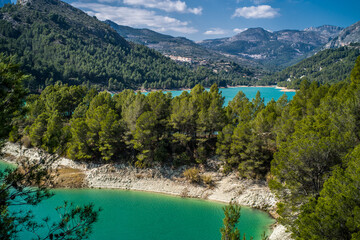 Lake Guadalest, rocky mountains and hills covered with trees. Blue sky