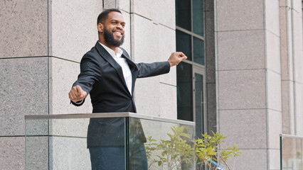 Happy funny cheerful African ethnic American male employee having fun entrepreneur businessman worker man on office balcony dancing celebrate business success winning corporate success with dance