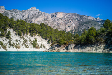 Obraz premium Lake Guadalest, rocky mountains and hills covered with trees. Blue sky