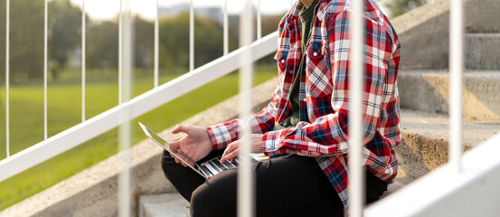 Non-binary appearance person sitting on the steps outdoors in park and working on laptop.