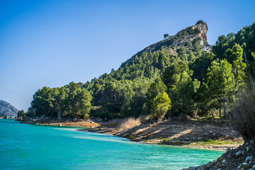 Naklejka premium Lake Guadalest, rocky mountains and hills covered with trees. Blue sky