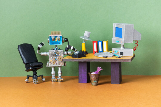 The robot office manager holds a telephone receiver in his hands. Retro workspace table, a personal computer, desk lamp and cases.