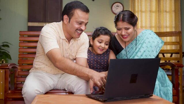 Happy smiling couple with daughter watching laptop while sitting on sofa at home - concept of technology, weekend holidays and relaxation