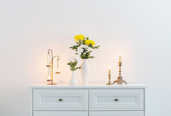 chrysanthemums flowers in vases and burning candles on white interior