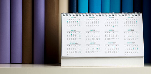 desk calendar with year 2024 and days, on shelf with books