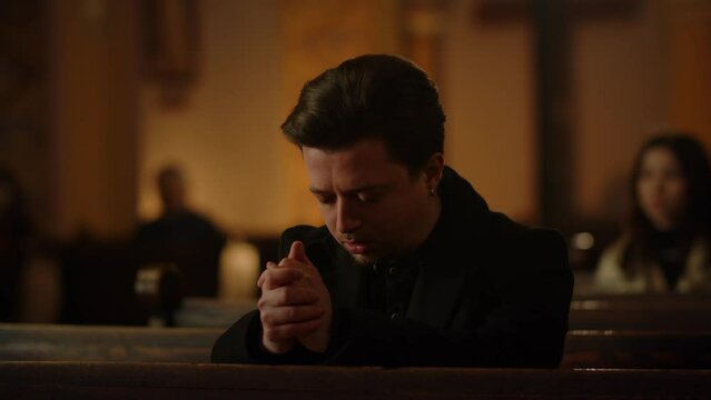 Young man praying in Church. Churchgoer praising God during Sunday Service. Religious man prays with closed eyes