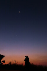 Women taking picture of nature observing evening sky with stars, planets and crescent moon. Moon meets Jupiter and Venus in the twilight sky. - obrazy, fototapety, plakaty