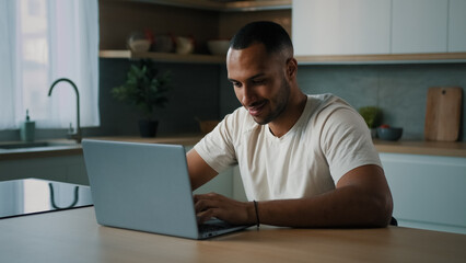 African millennial man multiracial guy American male user freelancer sitting at home kitchen desk using laptop working distant with computer app service online betting game chatting buying in Internet