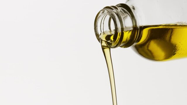 Side view macro shot of yellow oil is being poured from reagent bottle on white background | Abstract skincare cosmetics ingredients formulating concept