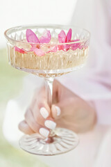 Champagne glass with pink petals of apple blossoms and a flowering branch on the background. A romantic unusual drink to celebrate.