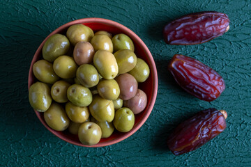 A bunch of date fruit with a bowl of green olives,on green background