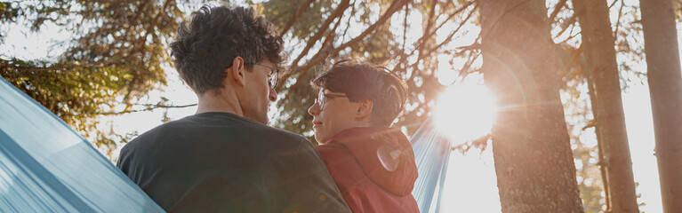 Back view on Caucasian happy man and woman in love sitting in hammock in forest and hugging.
