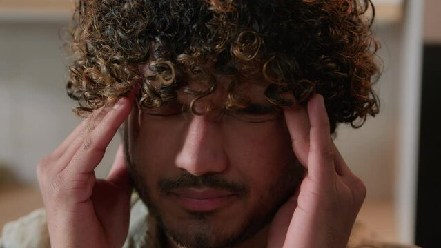 Close up sick tired Arabian male massage temples painful head migraine pressure head pain at home kitchen. Indian guy suffer with headache. Ill exhausted Indian man thinking difficult health problem