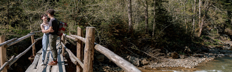 Couple in love standing on wooden bridge and hugging over fast river. Rural nature.