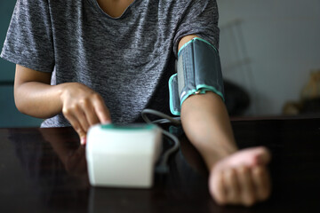Young  woman sitting on couch, checking blood pressure and taking notes at home. Midsection of Mature Woman Examining Blood Pressure At Home. Woman checking blood pressure