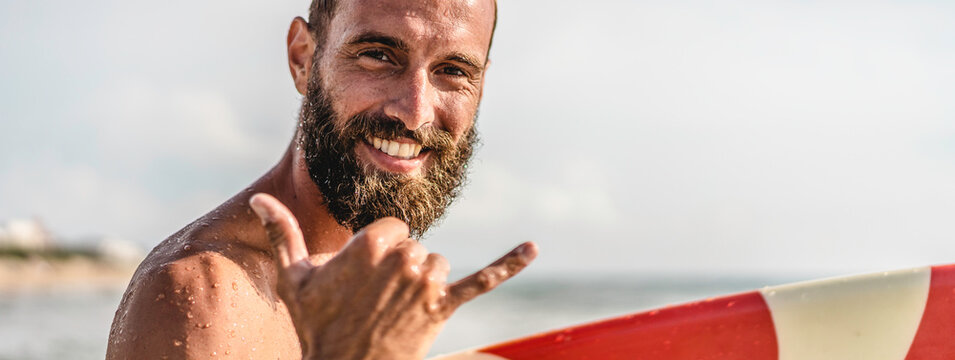 Horizontal banner or header with surfer happy with surf surfing smiling doing hawaiian Shaka Brah or Hang Loose during surf session in ocean waves on beach vacation - Greeting in surfer culture