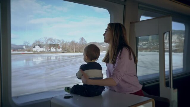A young woman and her baby enjoying a ride on a high-speed express train, admiring beautiful views from the window, exploring new places