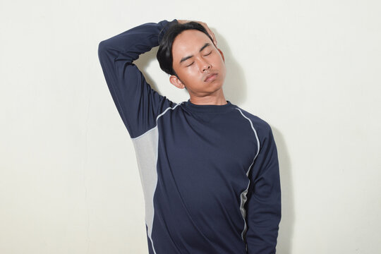 Asian Man Gesture Stretching Neck Or Warming Up. Indonesian Man Smiling And Looking At Camera Wearing Navy Sweater Or Sportswear On Isolated White Background. Portrait Of People Exercising