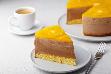Chocolate-orange mousse cake with biscuit base, jelly and orange circles. Piece of homemade cheesecake and a cup of coffee. Traditional holiday dessert. Selective focus, close-up.